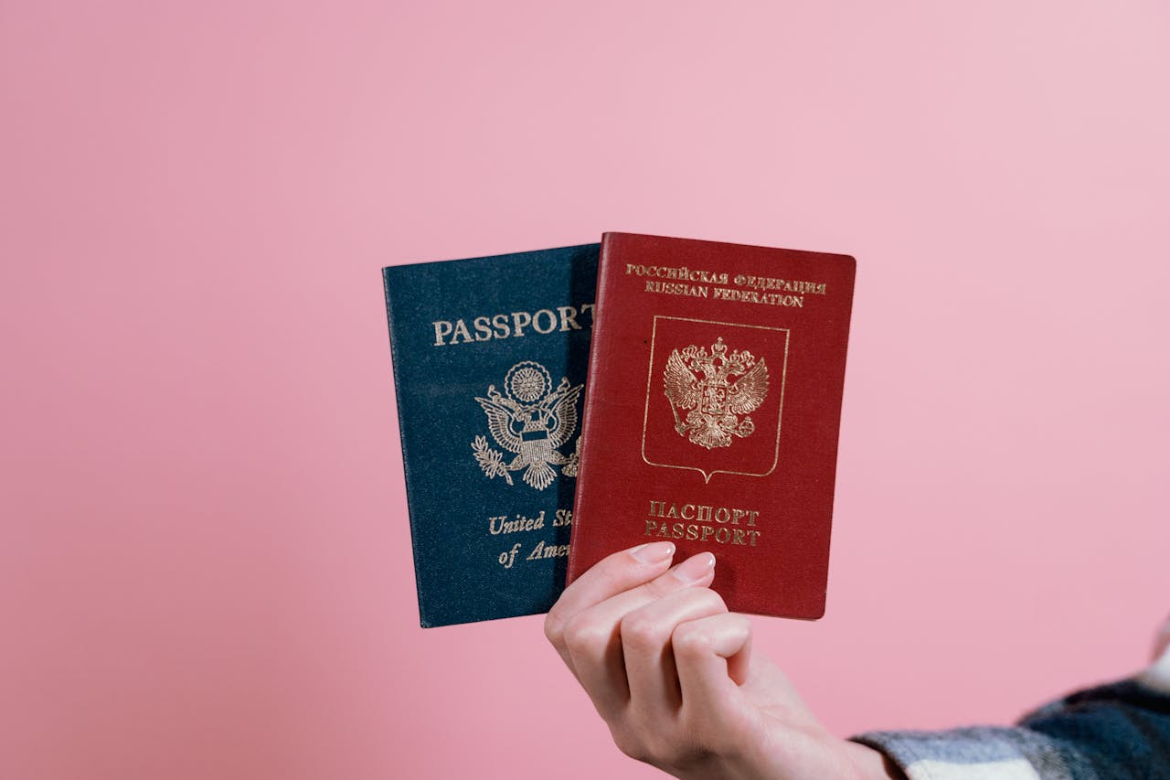 about-img Close-up of a hand holding American and Russian passports on a pink background.